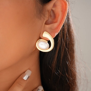 Close-up of golden spiral metal earring with an oval white pearl inlay on a female model