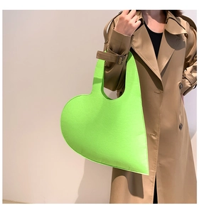 Detail of neon green heart-shaped felt tote bag held by model wearing khaki trench coat