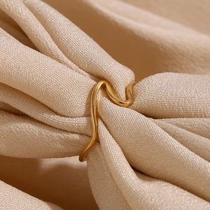 Macro shot of gold-plated wave ring detail highlighting polished texture on silk fabric