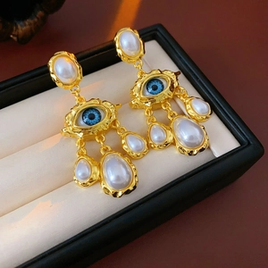 Detail of vintage gold earrings with blue evil eye design and dangling waterdrop pearls