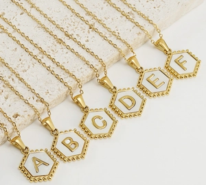 Close-up of hexagonal gold shell pendants with letters A to F on marble background