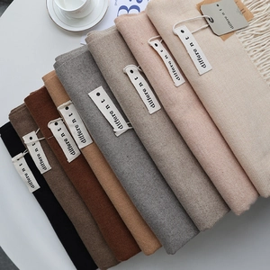 Close-up of stacked cashmere-style scarves with different brand labels and fringe details