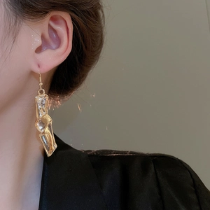 Close-up of a model wearing golden irregular twisted geometric long drop earrings