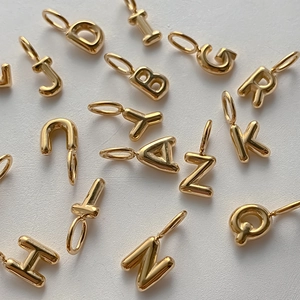 Close-up view of shiny 14K gold-plated bubble letter charms for DIY jewelry making.