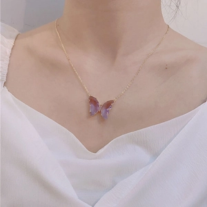 Detail of a purple crystal butterfly pendant on a gold chain worn by a female model