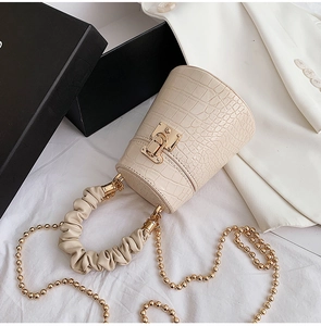 Detail of beige crocodile pattern bucket bag with ruched handle and gold chain strap