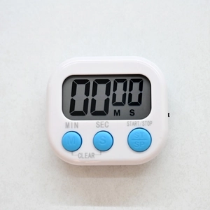 Macro shot of white digital timer with LCD screen and blue control buttons on countertop