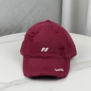 Detail of distressed burgundy baseball cap with white N embroidery and vintage torn effects