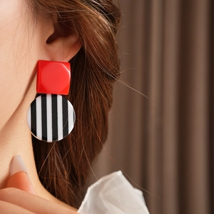 Close-up of geometric resin earrings with red square and black and white striped circle