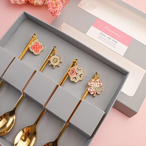 Close-up of four golden stainless steel spoons with decorative charms in a grey gift box