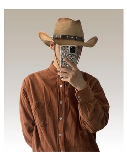 Close-up detail of a vintage straw cowboy hat featuring a studded brown leather band