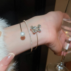 Macro detail of gold flower pearl cuff and zircon butterfly bracelet on a wrist