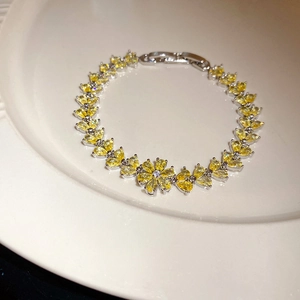 Detailed close-up of silver bracelet with yellow crystal flower in white ceramic dish