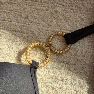 Close-up of black swimsuit detail with golden rings and inlaid white pearls