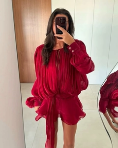 Detail of red pleated romper with pearl cuff buttons and ruffled hem design