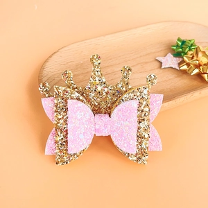 Detailed view of kids gold glitter crown and pink bow hair clip on a wooden tray