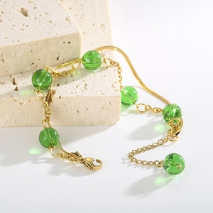 Detail of gold double-layer snake chain bracelet with green beads on beige stone