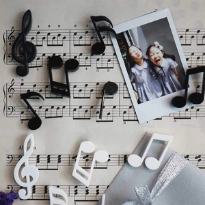 Creative music note fridge magnets in black and white shapes on piano sheet music