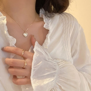 Golden heart necklace with pearl inlay and matching minimalist gold rings on model