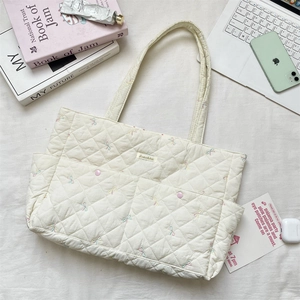 Detailed close-up of white quilted tote bag featuring floral embroidery and logo patch