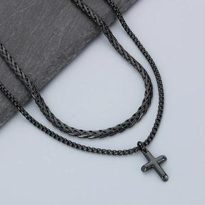Detail of a black layered cuban chain necklace with a cross pendant on a stone surface