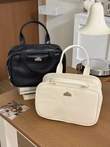 Detail of elegant black and cream PU leather toiletry bags with gold house logo on a desk
