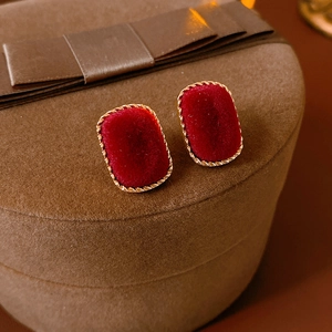 Close-up of red velvet rectangular earrings with gold woven border on a jewelry box lid