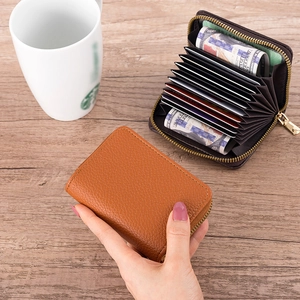 Close-up of caramel pebble leather accordion card holder with a gold zipper on a wooden table