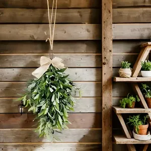 Artificial olive leaf garland with cream bow hanging on a rustic dark wooden wall background