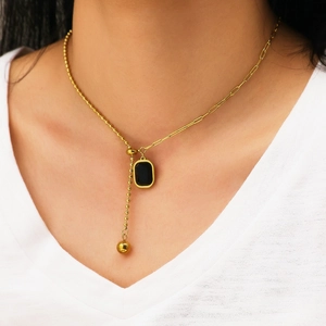 Detail of gold Y-shaped necklace with black rectangle gemstone on a model wearing white