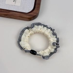 Detail of a beige fabric scrunchie featuring black plaid lace trim and a black bead accent