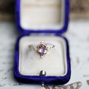 Macro shot of oval purple amethyst ring with diamonds in a blue velvet vintage jewelry box