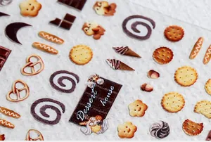 Vista macro di adesivi 5D per unghie con motivi di dessert, biscotti e cioccolato
