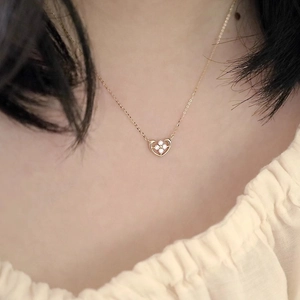 Close-up of a gold heart necklace with a clover zircon pendant worn on a model's neck
