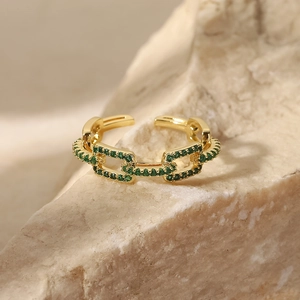 Detail shot of a 18K gold chain link ring with green zircon stones on a stone base