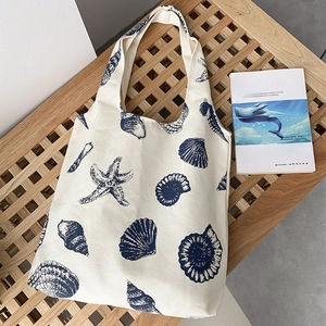 Detail of white canvas tote bag with blue starfish and seashell prints on wooden bench