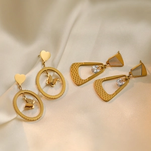 Golden butterfly and heart earrings with geometric pendants on beige silk background