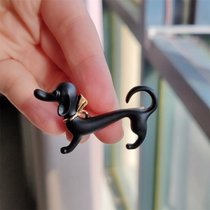 Close-up of cute black dachshund enamel pin with a gold bowtie being held by hand