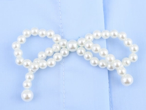 Detailansicht der eleganten weißen Perlen-Schleife auf hellblauem Hemdenstoff aus Baumwolle