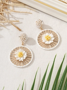 Macro detail of handmade bohemian raffia flower earrings with pearls and daisy center
