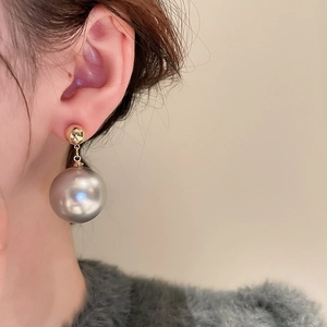 Close-up of elegant gold and silver pearl drop earrings worn by a model on a beige background