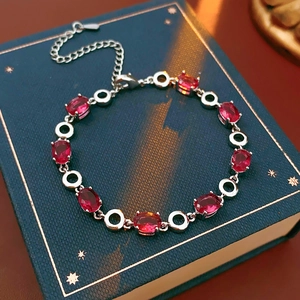 Detail of red oval-cut zircon bracelet with silver links on a vintage book background