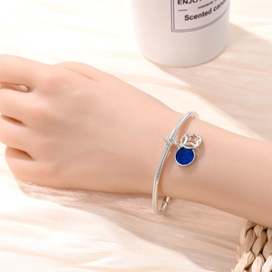 Detail of silver snake chain bracelet with blue enamel and star charms on wrist