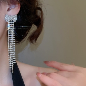 Macro shot of silver bow tassel earrings with sparkling rhinestones on model's ear