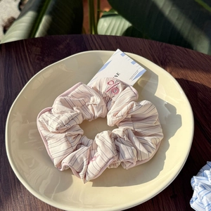 Detailed close-up of pink and white striped scrunchie with delicate embroidery in a tray