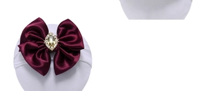 Detail of a dark red satin bow headband featuring a large gemstone and rhinestone center