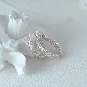 Detail of twisted silver hoop earrings on a white surface with ceramic flower decor
