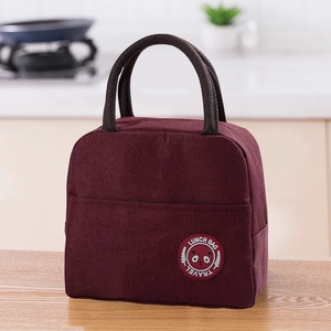 Close-up of wine red insulated lunch bag with woven handles on a wooden tabletop