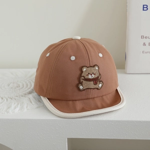 Detail of brown baby baseball cap featuring bear embroidery and floral eyelet accents