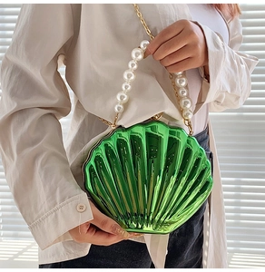 Detail of shell-shaped green metallic crossbody bag with pearl handle and gold chain